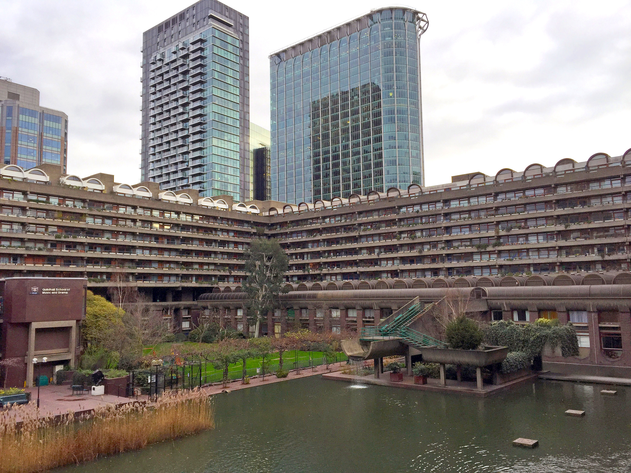 photograph showing two sides of the housing enclosure, a large water feature, and a park within the Barbican