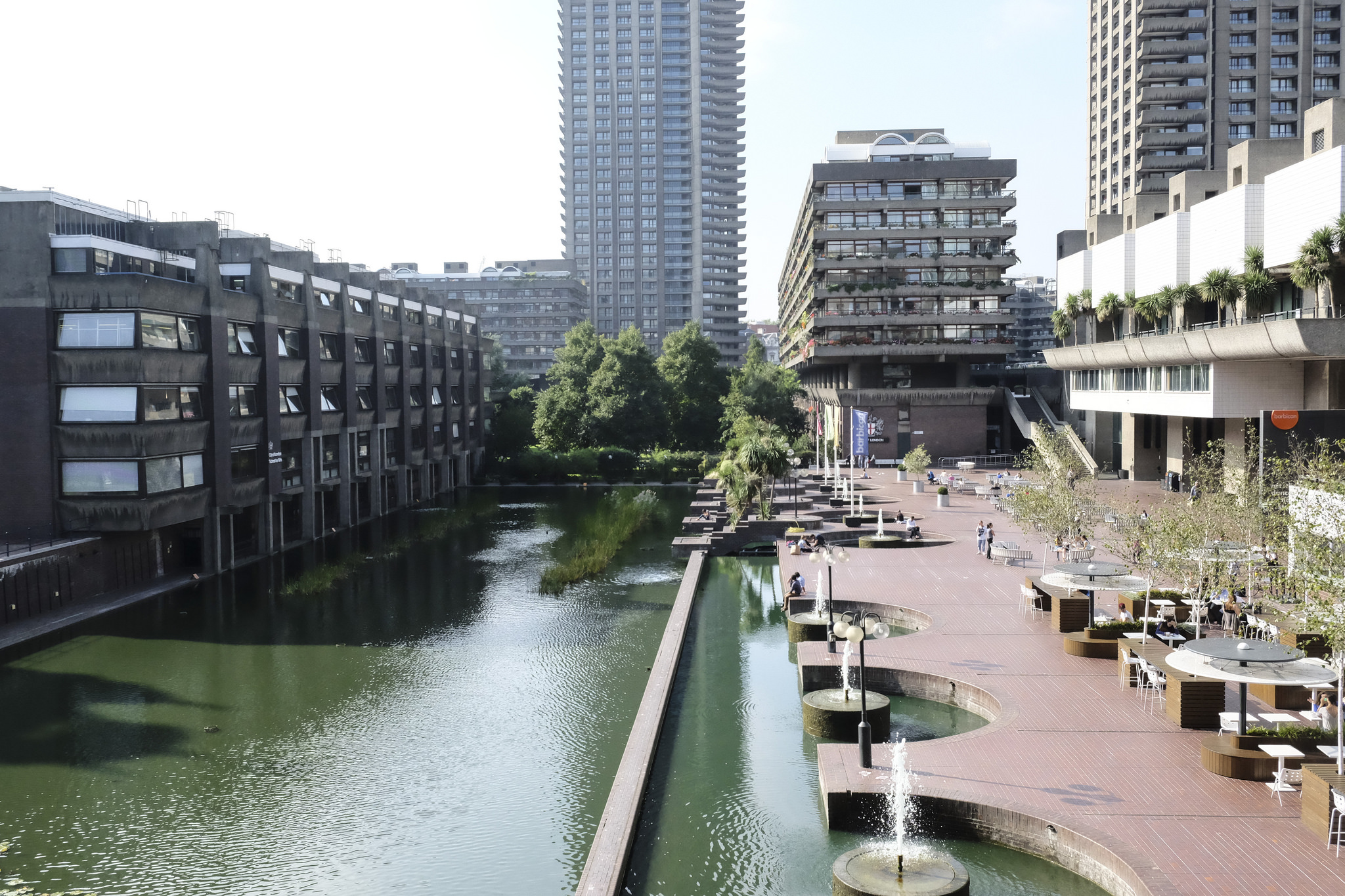 photograph of the Barbican showing a water feature, public seating and shopping, some housing, and the towers in the background