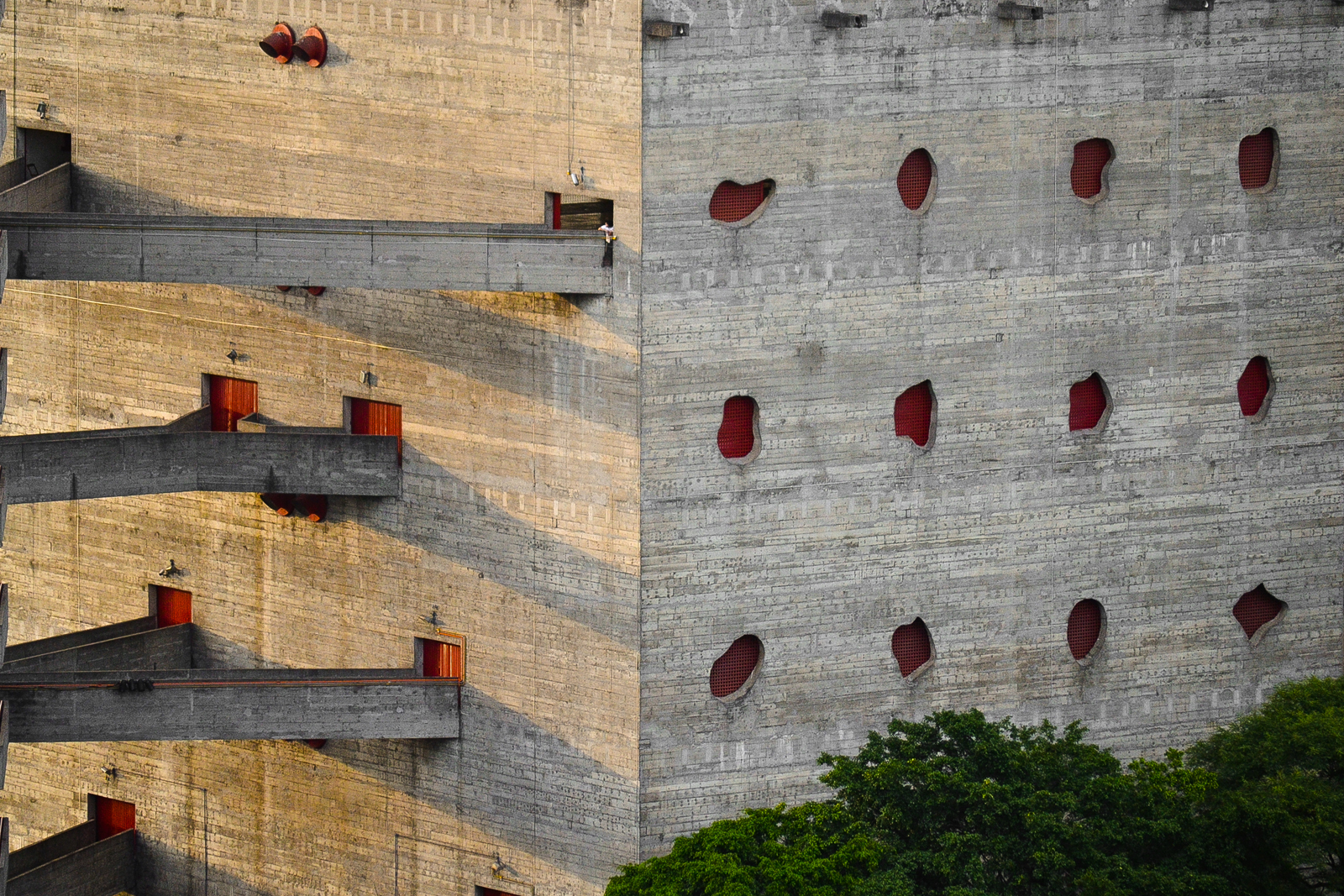 detail photograph showing the weathered concrete block construction, unusually shaped, red-gridded windows, and part of the split, angular skyways in the renovated SESC Pompeia factory